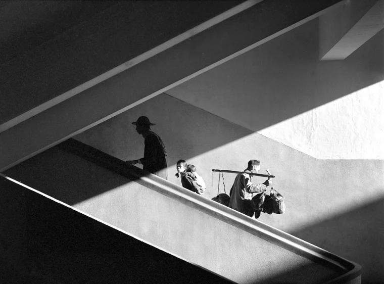 High-contrast black-and-white photograph with a strong diagonal of light and shadow, figures arranged along the line.