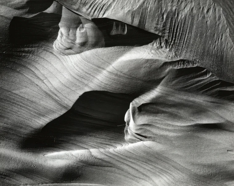 Near-abstract photograph of sunlit dunes, the frame divided into interlocking shapes of bright highlight and deep shadow.