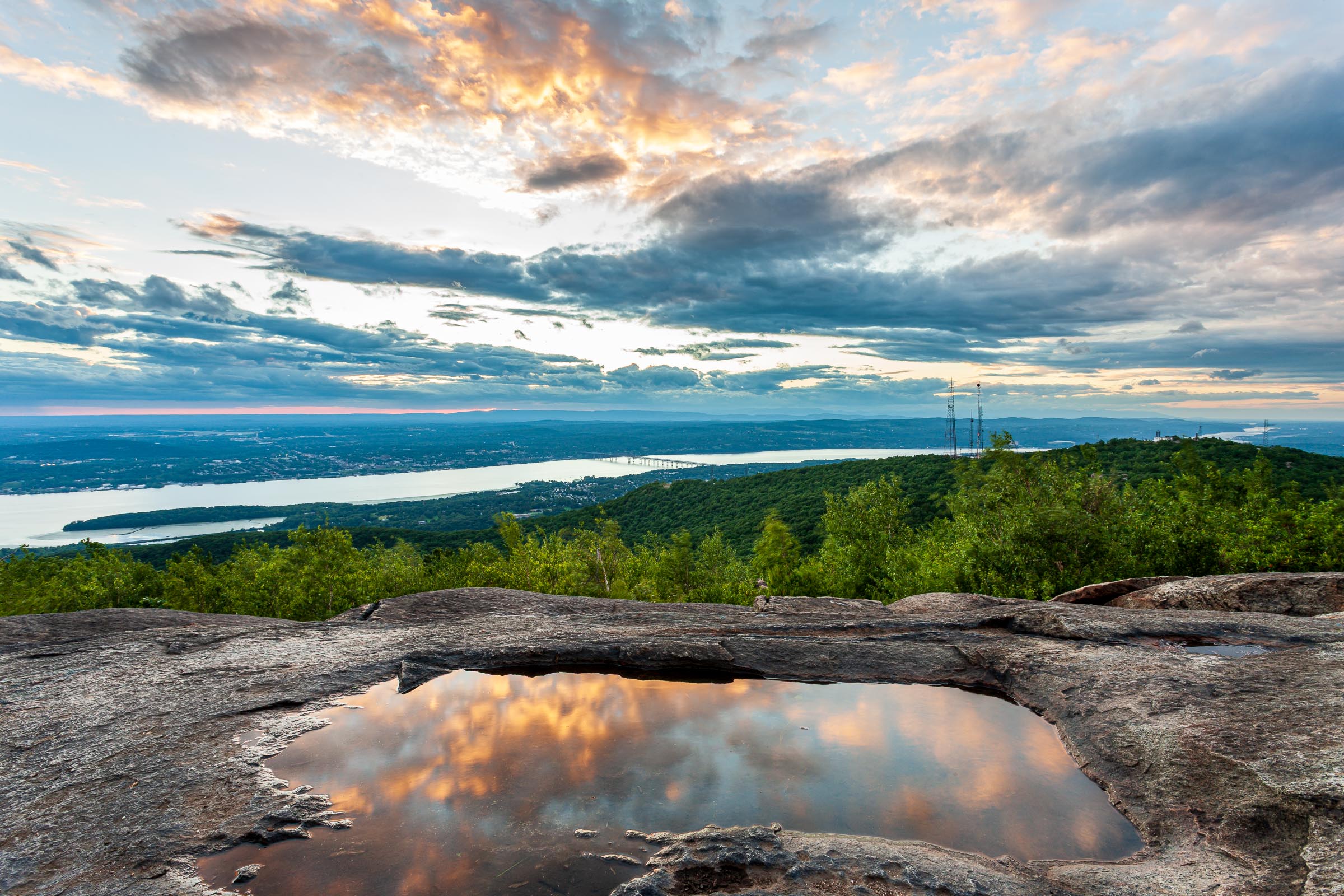 Sunrise clouds reflected in a rain pool on the rock summit of Mount Beacon, with the Hudson River below