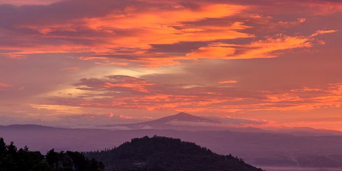 Glowing orange clouds above layered hills and a distant mountain at dawn